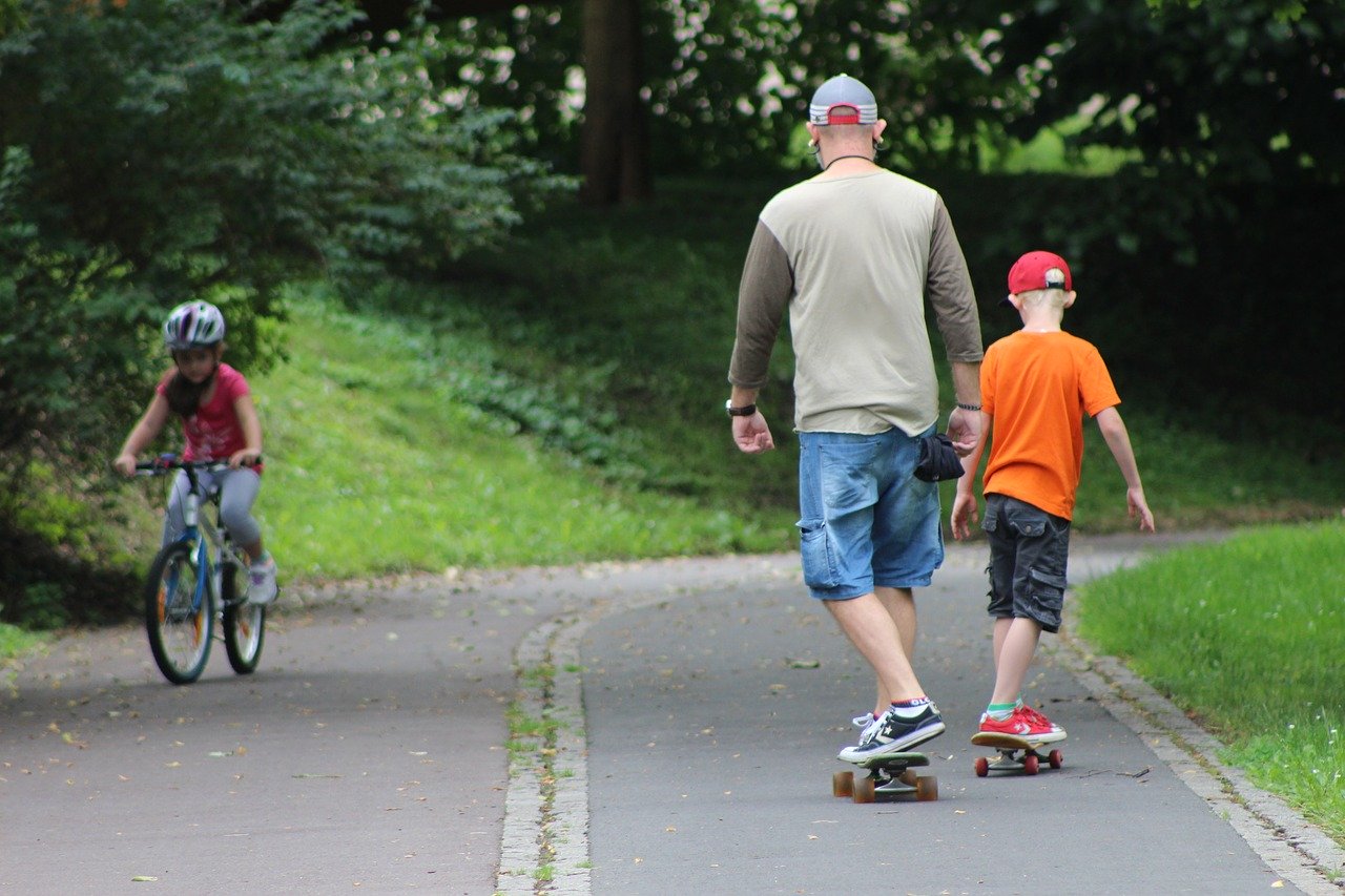 Man and boy on skateboards, with another child riding a bike